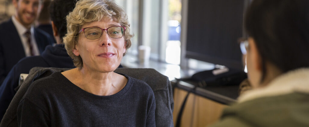 A mature woman listens to questions from a student. They talk across a table.